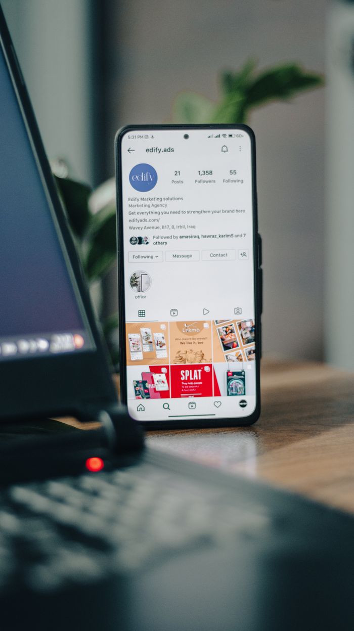 about-us-02 Vertical shot of a smartphone displaying an Instagram profile next to a laptop, representing social media engagement.